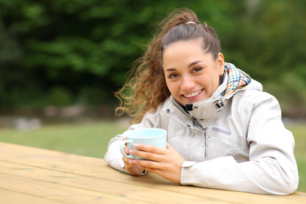 Marielle, bloggueuse bien-être, en train de boire un thé en pleine nature avec un manteau pour la pluie blanc