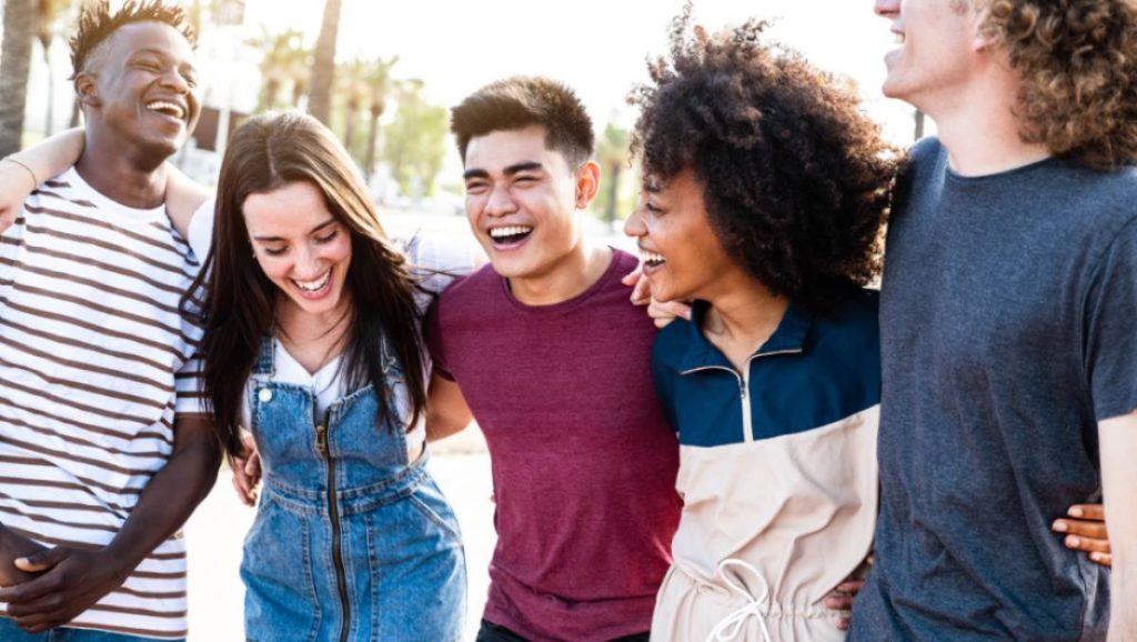 Groupe de 5 jeunes adultes se tenant par la taille dans la rue et en train de rigoler 